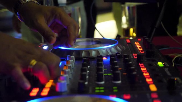 Close up of dj playing party music on modern cd usb player in disco club - Nightlife and entertainment concept. DJ turntable console mixer controlling with two hand in concert nightclub stage