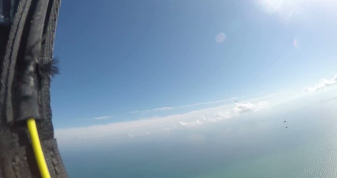 A base jumper in a wingsuit leaping off a from a rocky cliff, gliding down over a green landscape