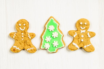 Gingerbread men friends at the Christmas tree on a white wooden table.