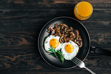 Vegetarian breakfast with fried eggs and mushrooms decorated with a rosemary sprig in a frying pan on a wooden table