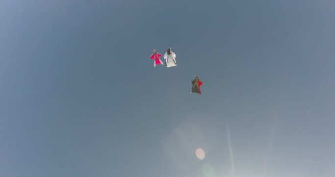 A base jumper in a wingsuit leaping off a from a rocky cliff, gliding down over a green landscape