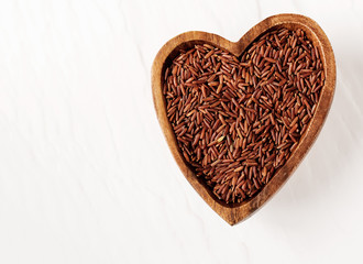 Isolated handful of raw red rice in the wood bowl in the shape of heart on black stone background