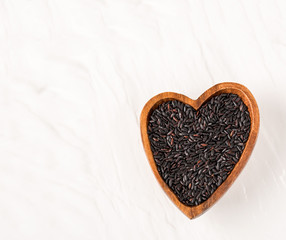 Isolated handful of raw black (nero) rice in the wood bowl in the shape of heart on white background