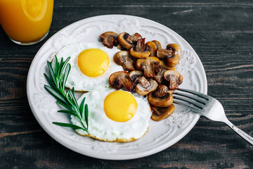 Vegetarian breakfast with fried eggs and mushrooms decorated with a rosemary sprig on a wooden table