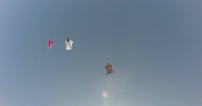 A base jumper in a wingsuit leaping off a from a rocky cliff, gliding down over a green landscape