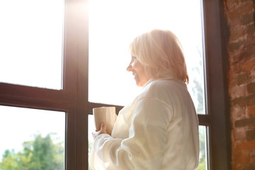 Morning of mature woman drinking coffee near window