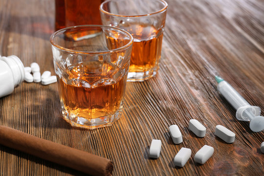 Composition with alcohol, cigar and drugs on wooden table. Concept of bad habits