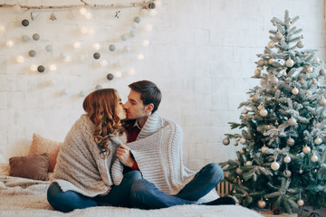 Naklejka premium Young couple kissing wrapped in a blanket on Christmas eve