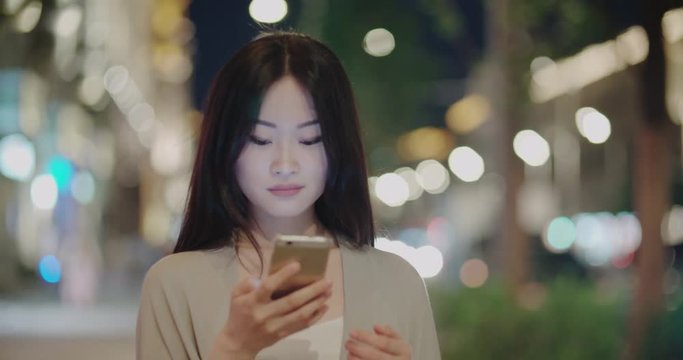 beautiful Asian girl is walking along a night megalopolis with a smartphone, uses the gadget for communicating,good mood with a smile, writes messages, Steadicam shot