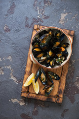 Wooden serving tray with a bowl of boiled mussels clams on a brown stone background, view from above with space