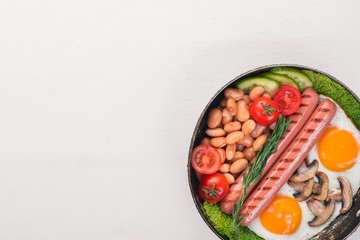 English breakfast tomatoes, sausages, beans, mushrooms, eggs,toast and herbs top view. On a white wooden background.