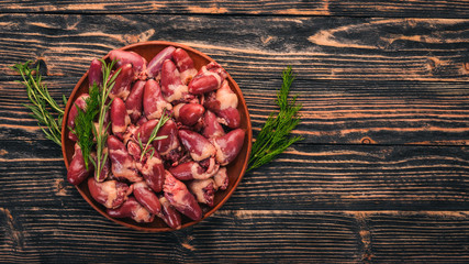 Raw chicken hearts on the plate ready for cooking with rosemary and spices on a black wooden background. Top view. Free space for text.