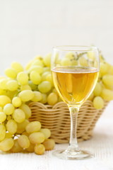 Glass of wine and grapes in the basket on a wooden table.