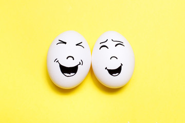 Two eggs with drawn laughing faces on yellow background