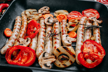 Appetizing grilled sausages and vegetables served in a frying pan with sauce and spices, close up. Grill menu, kitchen background, restaurant concept