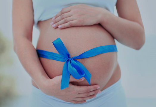 woman holding hands on her baby bump, tied with a blue bow