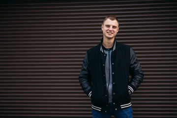 Fototapeta premium A young guy in a black jacket against a background of dark striped walls posing and smiling at the photographer