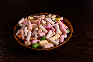 Ceramic dish with the different multi colored candies on a dark wooden table