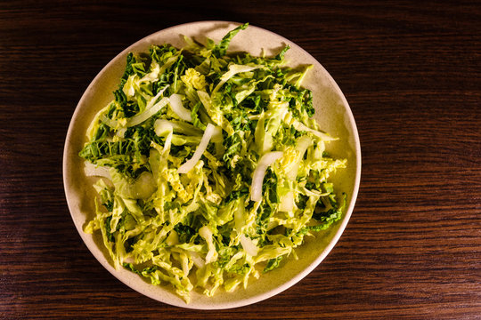 Salad with the savoy cabbage in the dish on dark wooden table. Top view