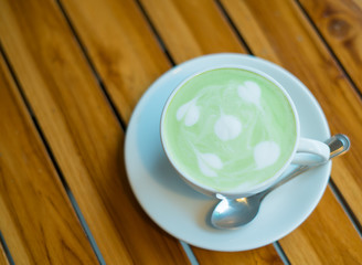Selective focus.Hot matcha green tea latte with milk foam in a white cup and plate on old wooden table.