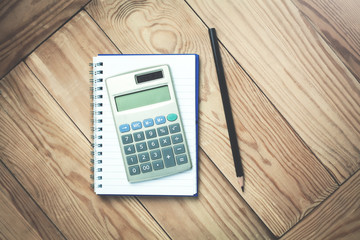 Calculator with notepad and black pencil on a wood background.