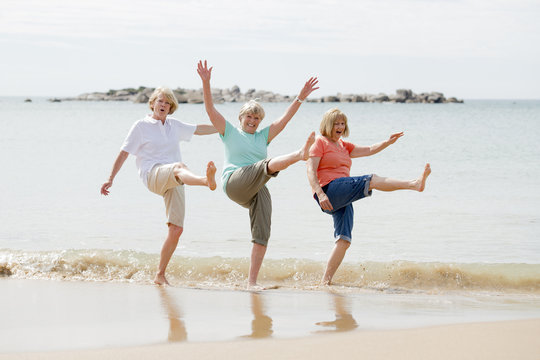 group of three senior mature retired women on their 60s having fun enjoying together happy walking on the beach smiling playful