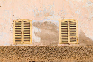 Two symmetrical run down rustic brown and cream shutters on windows in Santa Maria, Sal, Cabo Verde, Africa.