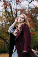 portrait of a luxurious, beautiful, young girl. Dressed in stylish clothes, walking in an autumn park. Bright lipstick on the lips.