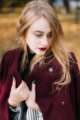 portrait of a luxurious, beautiful, young girl. Dressed in stylish clothes, walking in an autumn park. Bright lipstick on the lips.