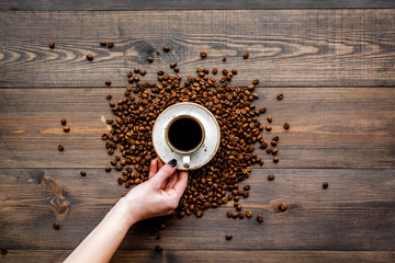 Hand hold cup of freshly brewed full-bodied coffee on dark wooden table top view. Coffee background.