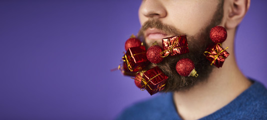 Closeup of Handsome man with tiny red gift box in beard on purple background. Space for text