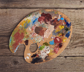Drawing tools in art studio. Palette with oil paints brushstrokes mixture. Artist old wooden table with accessories. Creative concept