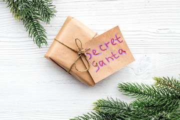 Christmas game Secret Santa. Gift box near spruce branch on white wooden background top view copyspace