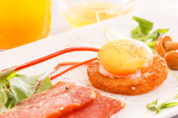Breakfast with poached egg on crispy toast with mushrooms, ham and greens. Fresh juice, sauce. Low morning light