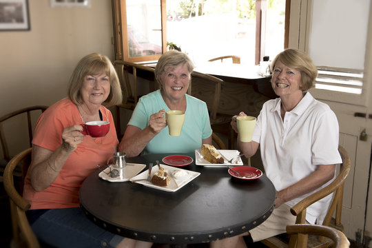 group of three lovely middle age senior mature women girlfriends meeting for coffee and tea with cakes at coffee shop sharing time together