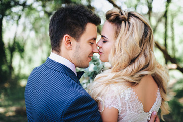 A beautiful blond bride gently kisses the nose of her groom. Faces of loving newlyweds in profile.