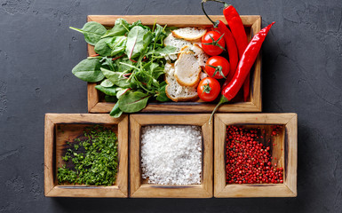 Woman holding cooking ingredients and herbs in wooden box on dark background