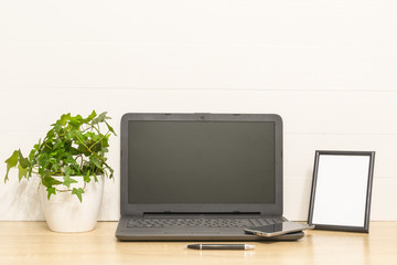 Fototapeta premium Laptop on wooden table with photo frame, ivy plant in pot, pen, smart phone. Working space in loft. Interior photo