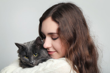 Beautiful young woman holding cat on grey background