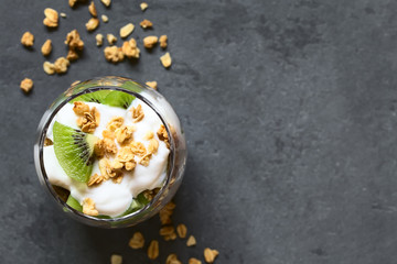 Yogurt parfait with fresh kiwi and crunchy almond and oatmeal granola in glass, photographed overhead on slate with natural light (Selective Focus, Focus on the top of the parfait)