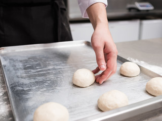 Baker works with dough on a metal work surface. Professional cook making rolls or buns