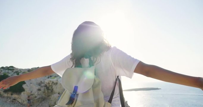 Portrait of a beautiful young tourist (girl), in a white dress, looks, with a backpack, in a straw hat, walking along rocks, sea background and mountains. Concept: recreation, beautiful view, sports.