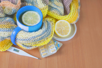 Concept illness, colds, cure, fall and winter. Tea with lemon, thermometer, pills and a knitted...