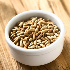 Roasted sunflower seeds in small bowl, photographed on wood with natural light (Selective Focus, Focus in the middle of the seeds)