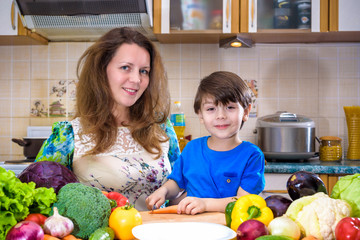The young cook mother standing with her little son in the kitchen and salting vegetables