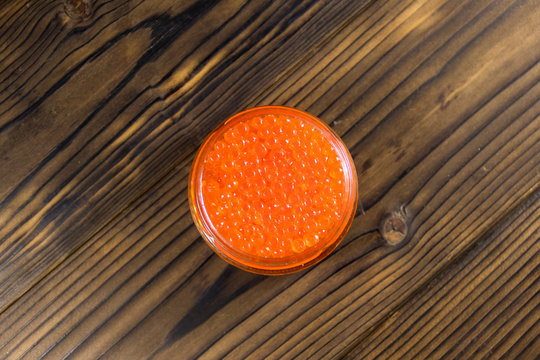 Red caviar in glass jar on wooden table