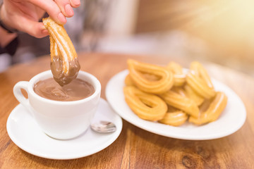 female hand dipping churro into hot chocolate