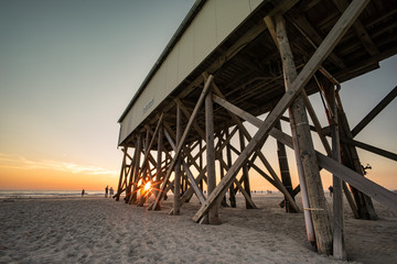Nordseeurlaub -Sonnenuntergang am Strand von St. Peter Ording, typischer Stelzenbau aus Holz