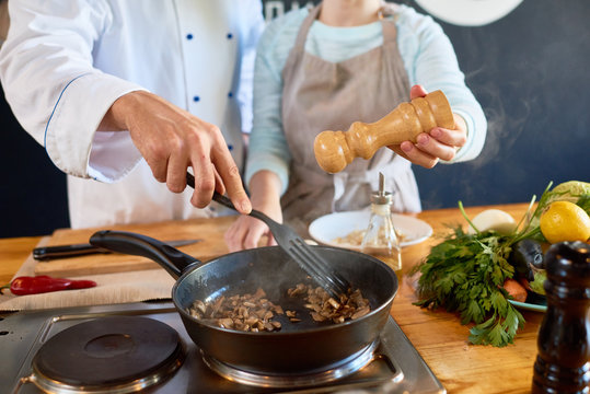 Close up of two unrecognizable chefs working in kitchen, roasting mushrooms and adding salt and pepper in modern open kitchen