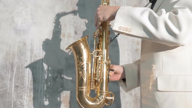 A musician in a white suit plays the saxophone. He performs in a nightclub, against a gray background. close-up